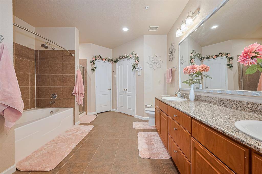 This generously sized bathroom features a dual-sink vanity with a wide mirror and elegant lighting. A shower/tub combo sits alongside a separate glass-enclosed shower—perfect for any routine.