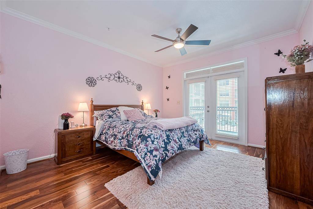 Crowned with molding and set on the same rich wood flooring, this spacious bedroom offers direct balcony access through glass-paneled double doors. A ceiling fan completes the inviting ambiance.