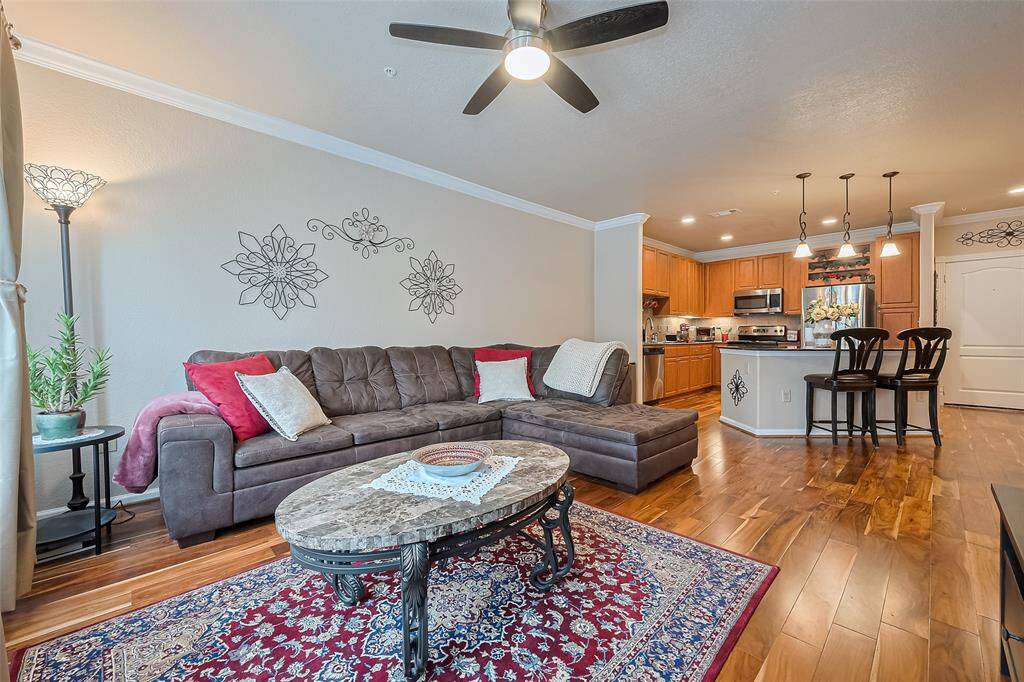 The living area flows seamlessly into the kitchen, unified by crown molding and warm wood flooring. This open-concept layout is ideal for both quiet evenings and casual entertaining.