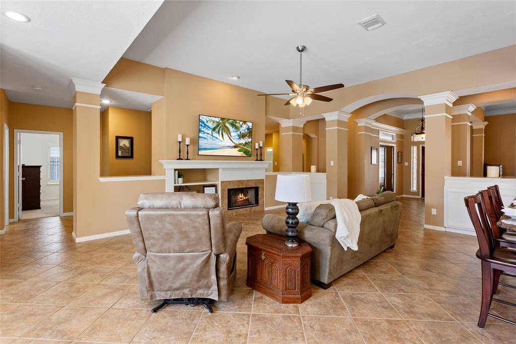 This spacious living room features soaring ceilings and a cozy fireplace. The unique design of this home allows you to walk down the hallway behind the fireplace and TV with openings to the living room.  Elegant columns, archways and crown molding add a touch of sophistication.