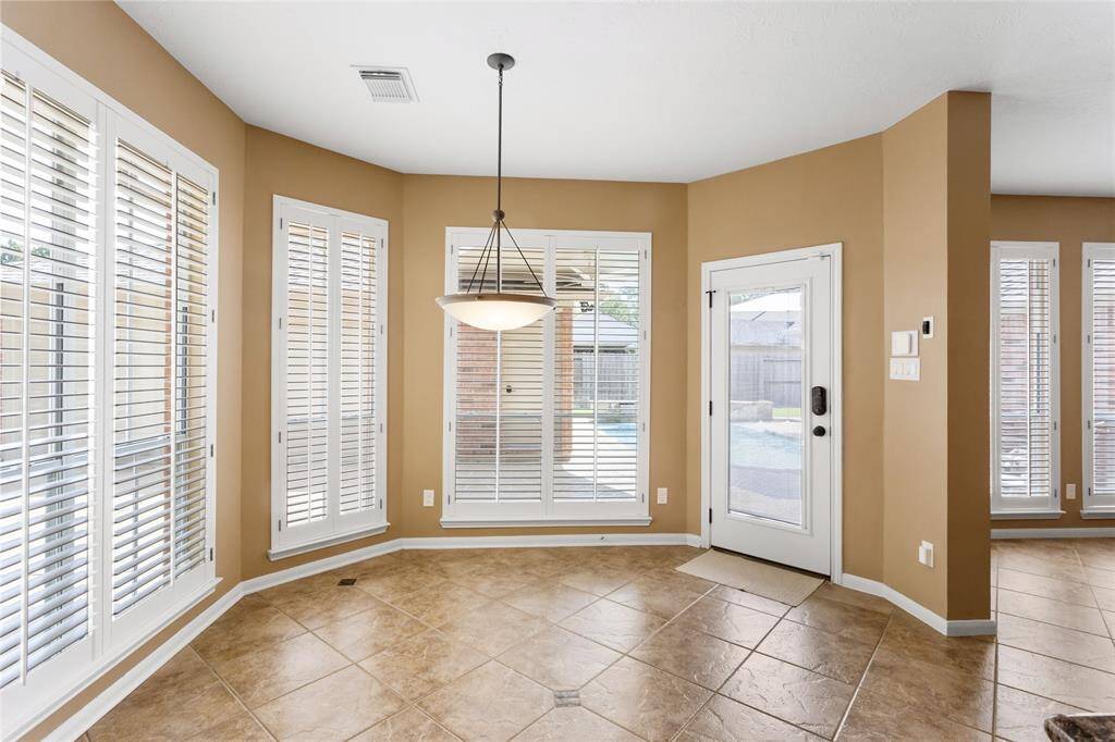 Bright breakfast nook with large windows featuring wooden plantation shutters, tile flooring, and a central light fixture. The space opens to the backyard patio and pool, enhancing indoor-outdoor flow.