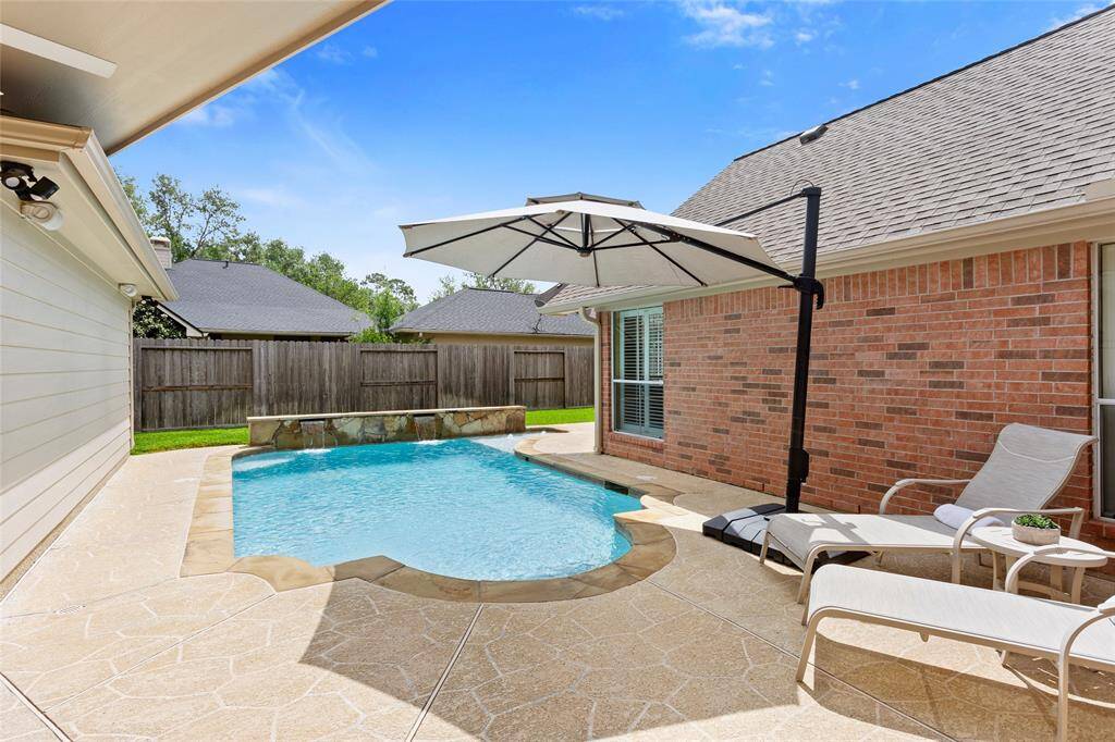 This beautiful backyard features a wrap-around pool with sundeck and a stone fountain, surrounded by a pool deck. This area is perfect for relaxing and enjoying sunny days.