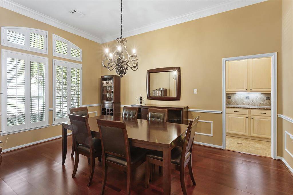 The elegant dining room has warm-toned walls, hardwood floors crown molding and large windows with wooden plantation shutters.