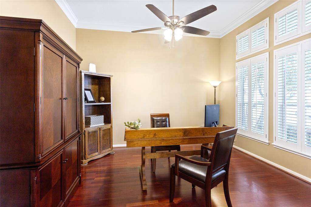 Inviting home office space featuring rich wood flooring, crown molding, and a large window with shutters allowing ample natural light.