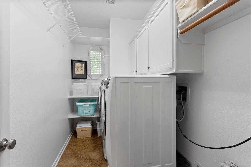 The oversized laundry room features overhead cabinets, wire shelving, and a small window for natural light. Shelves on the side provide additional storage space for baskets.