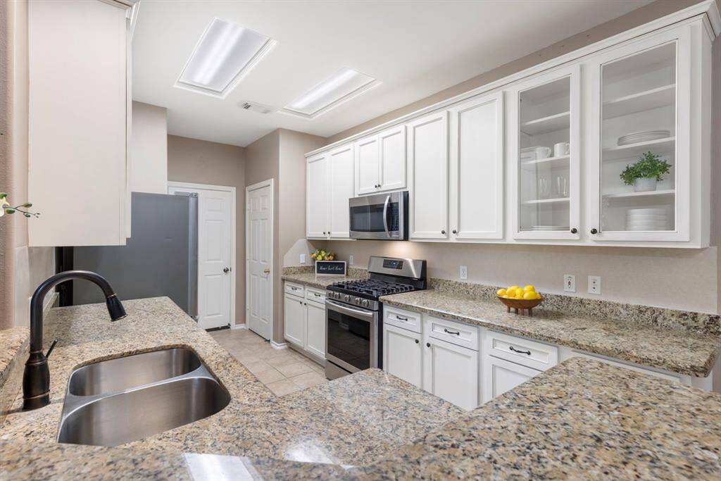 The kitchen is light and bright, featuring a new gas stove/oven combo, stainless steel appliances, and elegant glass cabinetry.