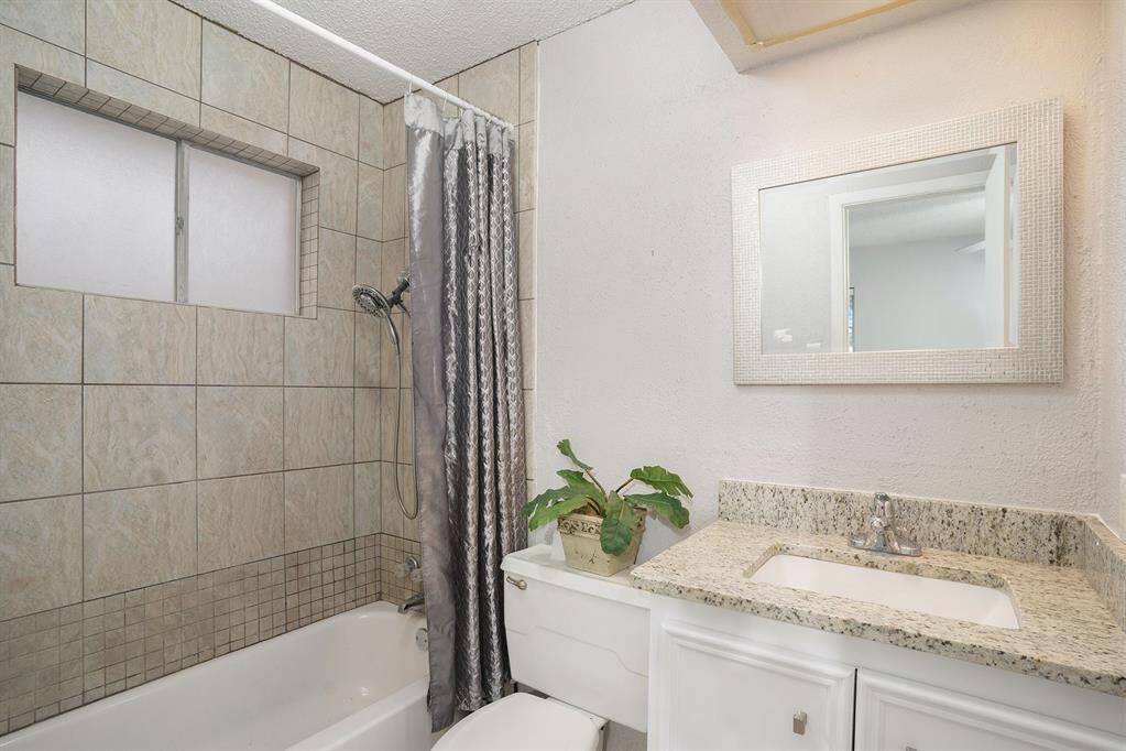 This bathroom features a tiled shower with a window for natural light, a sleek granite countertop with an undermount sink, and a clean, modern design.