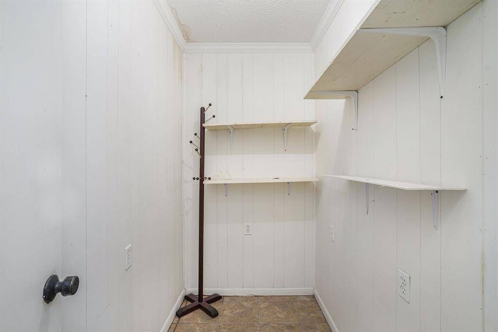 This is a small storage or utility room with white paneled walls, a few wall-mounted shelves, and a coat rack. The floor is tiled, and the space is simple and functional, ideal for organizing household items.