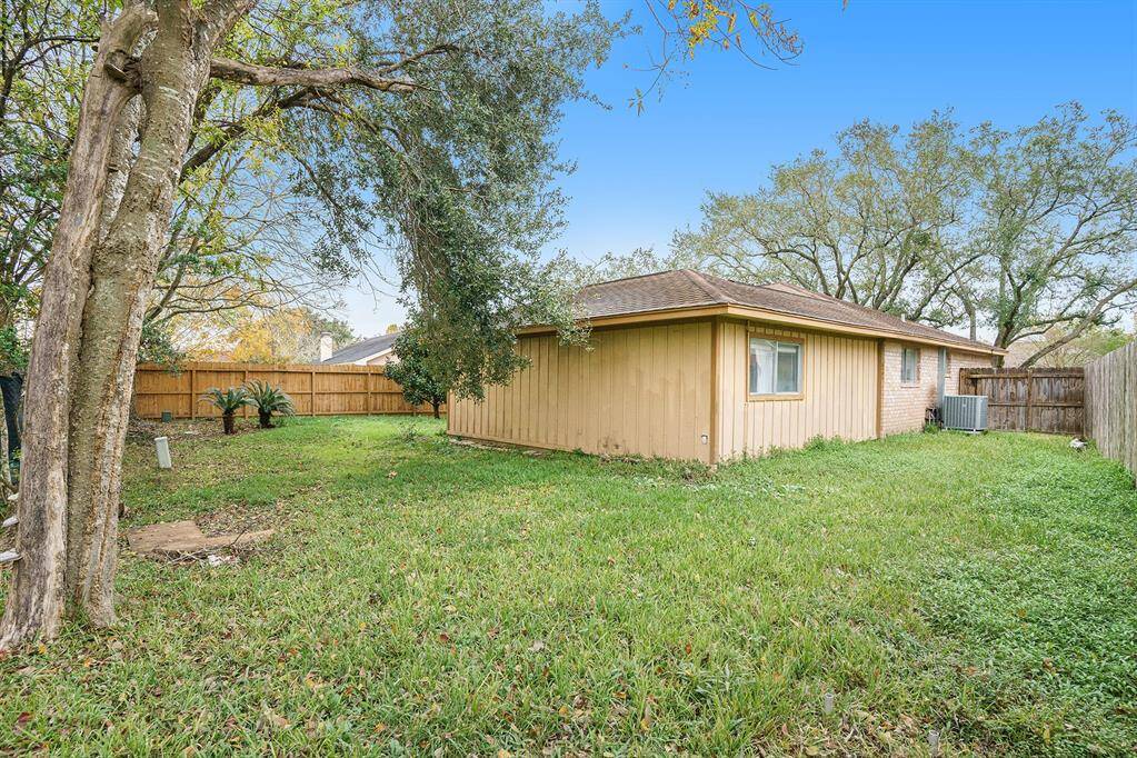 This photo shows a cozy backyard with a grassy lawn, mature trees, and a fenced perimeter. The house is a single-story structure with a wooden exterior, offering a private and serene outdoor space.