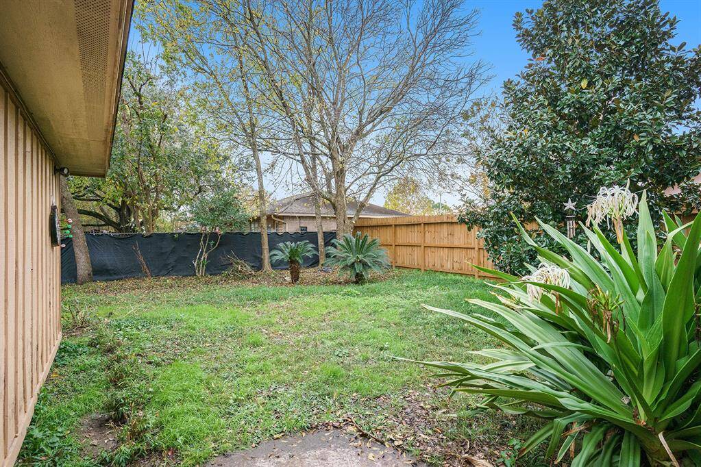 This backyard features a cozy, fenced space with mature trees and lush greenery, providing privacy and a natural setting for outdoor activities.
