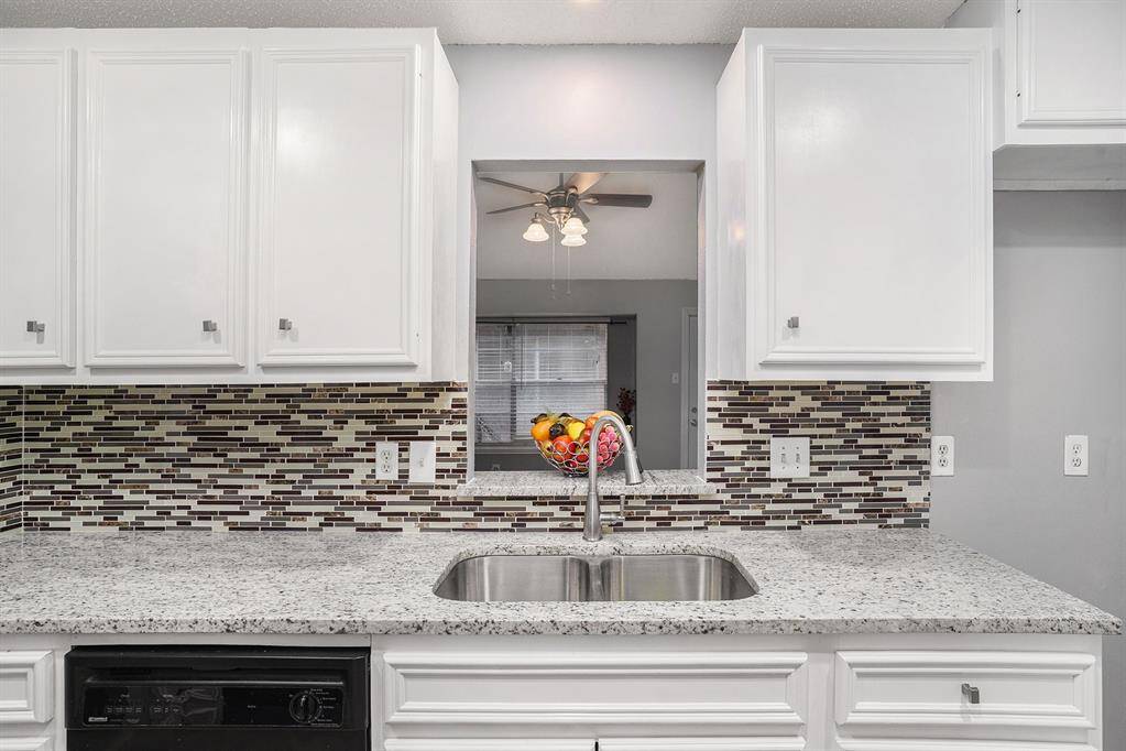 This photo showcases a modern kitchen with white cabinets, a sleek mosaic tile backsplash, and granite countertops. It features a stainless steel sink and a pass-through window, adding openness and natural light.