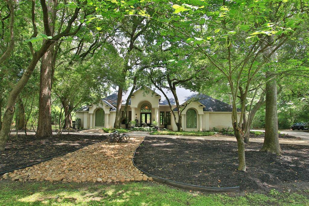 This photo features a charming single-story home nestled among mature trees, offering a sense of privacy and tranquility. The house has a welcoming front entrance with large windows and a well-maintained landscape, including a neat rock pathway and lush greenery. Perfect for those seeking a serene, nature-surrounded living space.