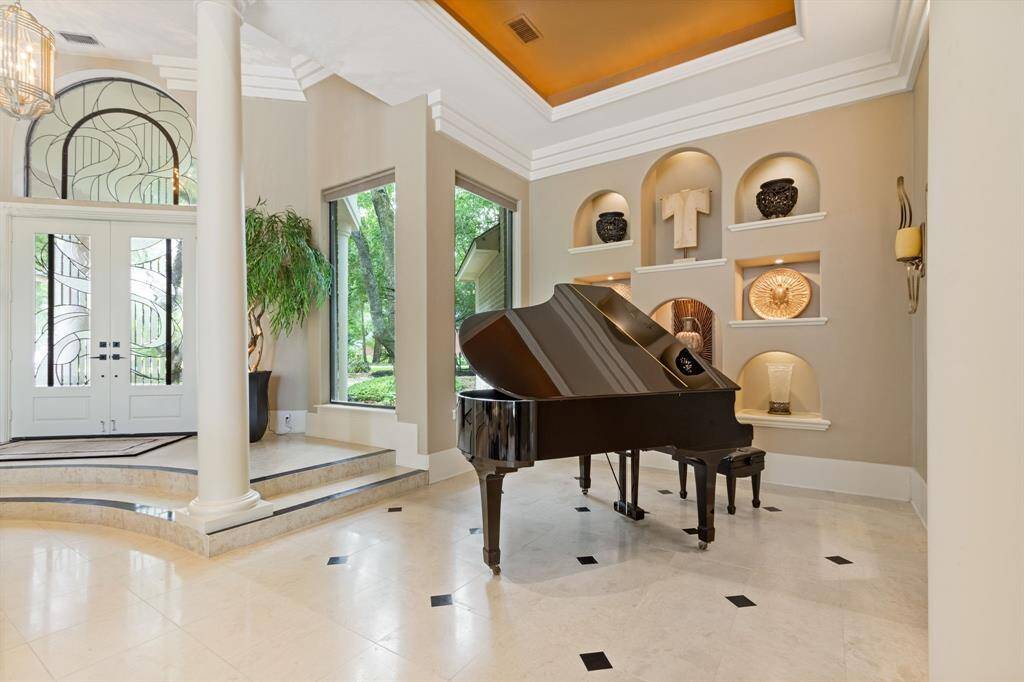This elegant living space features high ceilings, and large windows that offer ample natural light. The entryway showcases decorative glass doors and an artistic alcove wall, creating a sophisticated ambiance.