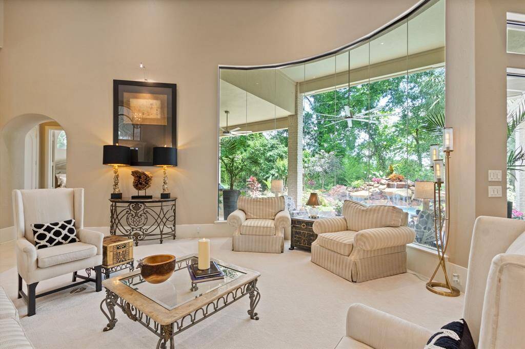 Experience elegance in this living room with expansive curved windows showcasing breathtaking views of lush greenery and a serene pool. Ideal for entertaining your guests in the open floor plan.