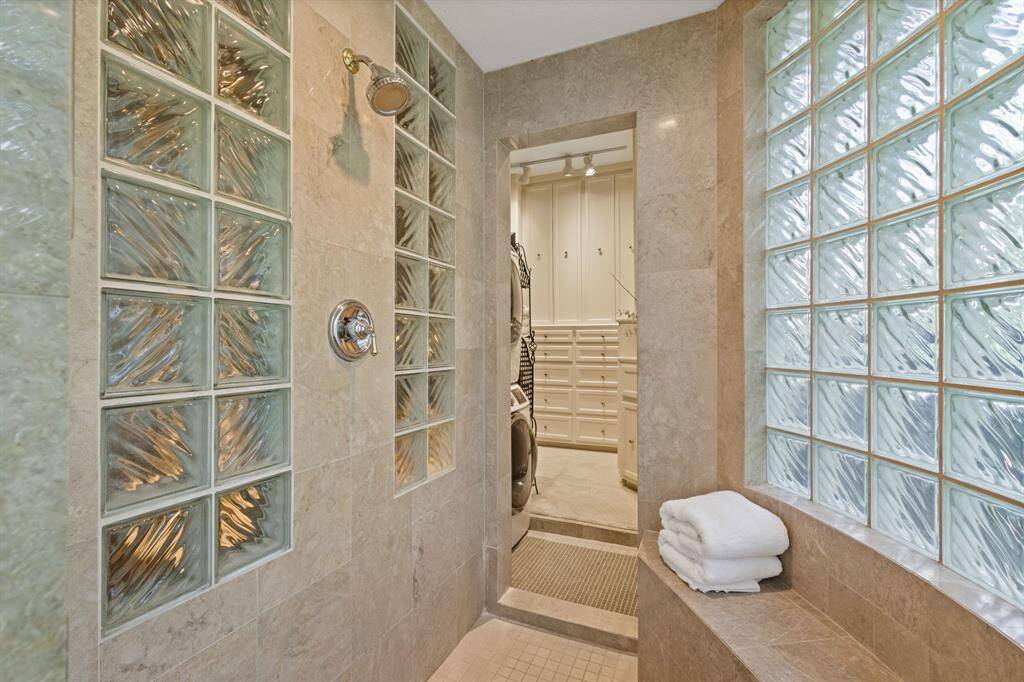 Experience luxury with this spacious walk-through shower, featuring bench seating and a large shower head. It seamlessly connects to a private utility area and dressing space.