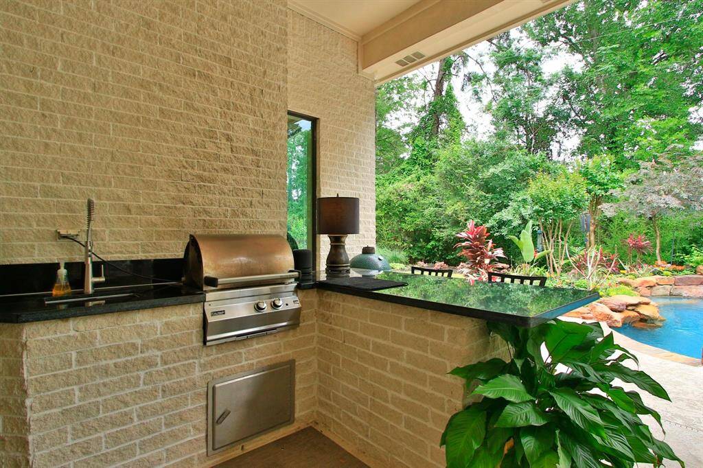This outdoor space features a built-in grill and sink with a sleek black countertop, perfect place for entertaining. It overlooks a lush garden and a sparkling pool, creating a serene and inviting atmosphere.