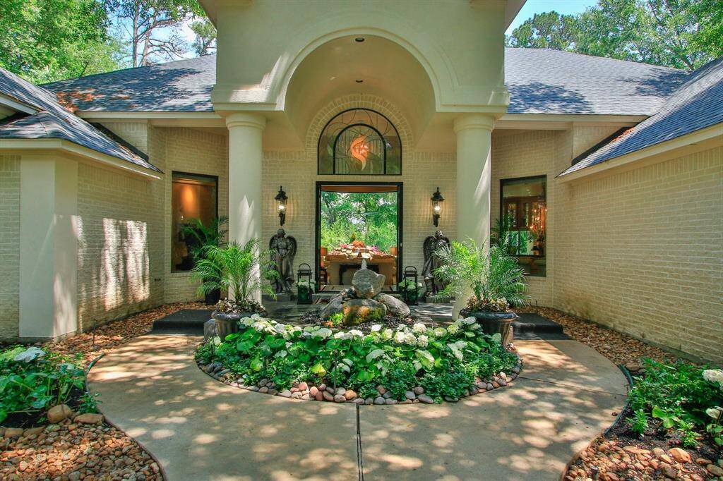 This elegant home features a grand entrance with a landscaped walkway, lush greenery, and a decorative fountain centerpiece, framed by white brick and large columns for a welcoming and luxurious curb appeal.