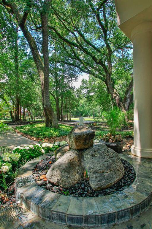 This photo showcases a serene, landscaped garden with mature trees providing ample shade. A unique rock fountain adds a focal point near a curved pathway, creating a tranquil outdoor space ideal for relaxation and nature enjoyment.