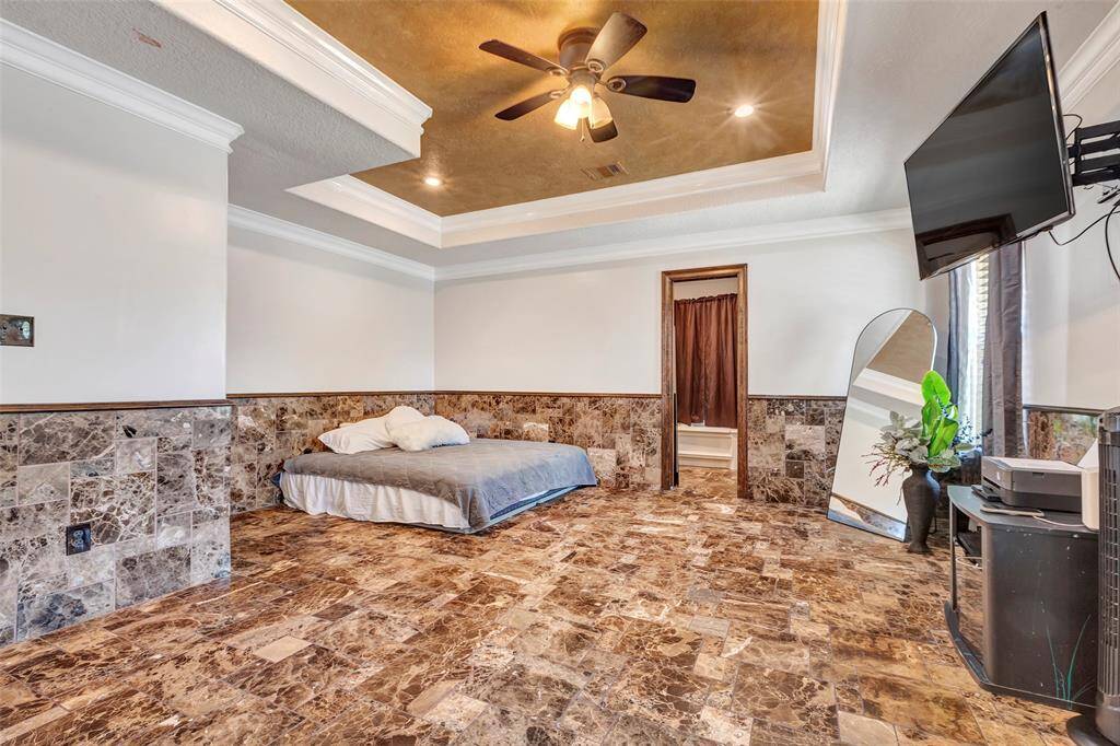 The main suite offers a luxurious retreat with striking tray ceilings and  elegant marble tile flooring