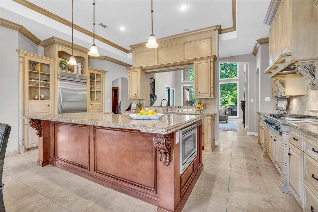 Gourmet kitchen showcases an immense, furniture-style island, pendant lighting, and built-in microwave, flanked by custom 42in glazed cabinetry and KitchenAid refrigerator that stays.