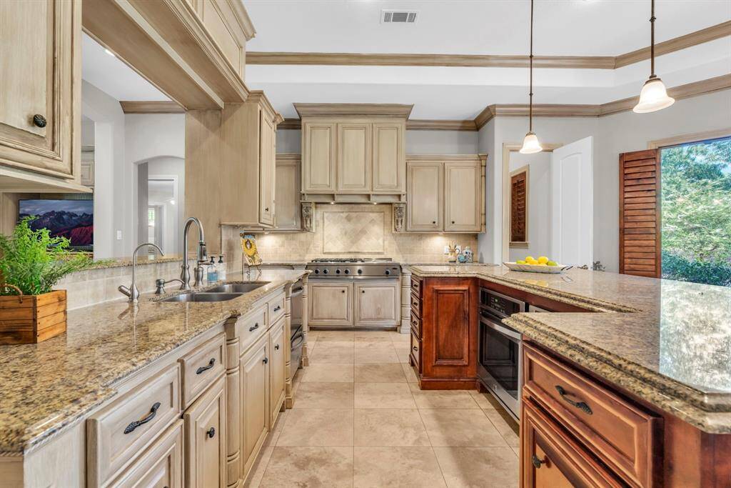 Chef-caliber kitchen workstation featuring a professional 5-burner gas range with center griddle beneath a custom vent hood, flanked by double ovens and twin dishwashers for seamless prep and cleanup. The oversized sink includes built-in water filtration, while plantation-shuttered windows in the adjoining breakfast area bathe the space in soft, filtered light.