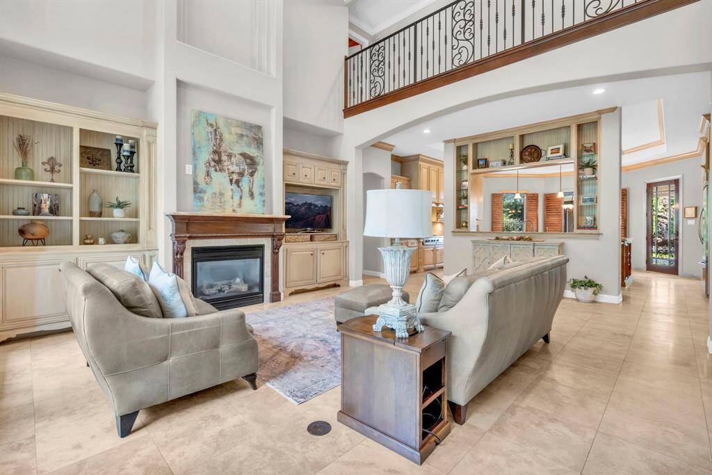 Grand living room featuring a two-story ceiling, iron catwalk, built-in media cabinetry, and a dignified wood-mantel fireplace—seamlessly open to the chef’s kitchen.