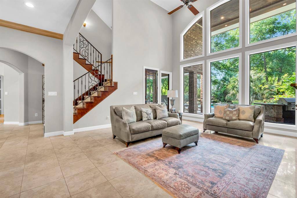 Breathtaking wall of windows floods the living space with natural light and frames lush pool views; note the elegant iron-spindled staircase and direct patio access.