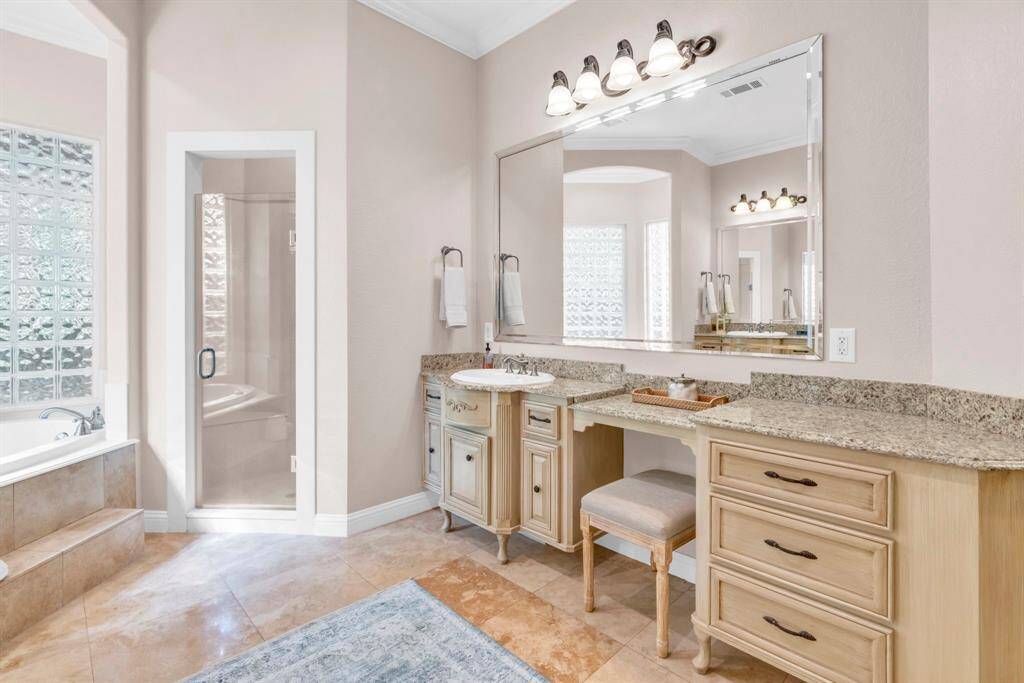 Spa-inspired primary bath offers dual vanities with seating area, granite counters, and a frameless glass shower