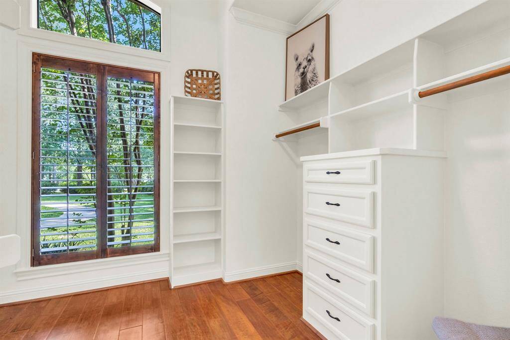 One of the boutique-style primary closets showcasing custom built-ins, drawer stack, open shelving, and a window with plantation shutters—natural light meets impeccable organization.
