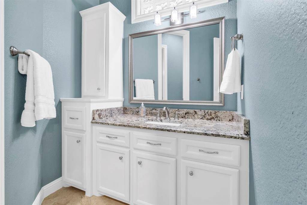 First of two private vanity stations in the Hollywood bath—complete with granite counter, framed mirror, and linen tower—connected by a centrally located water closet with stand-up shower shared between the two bedrooms.