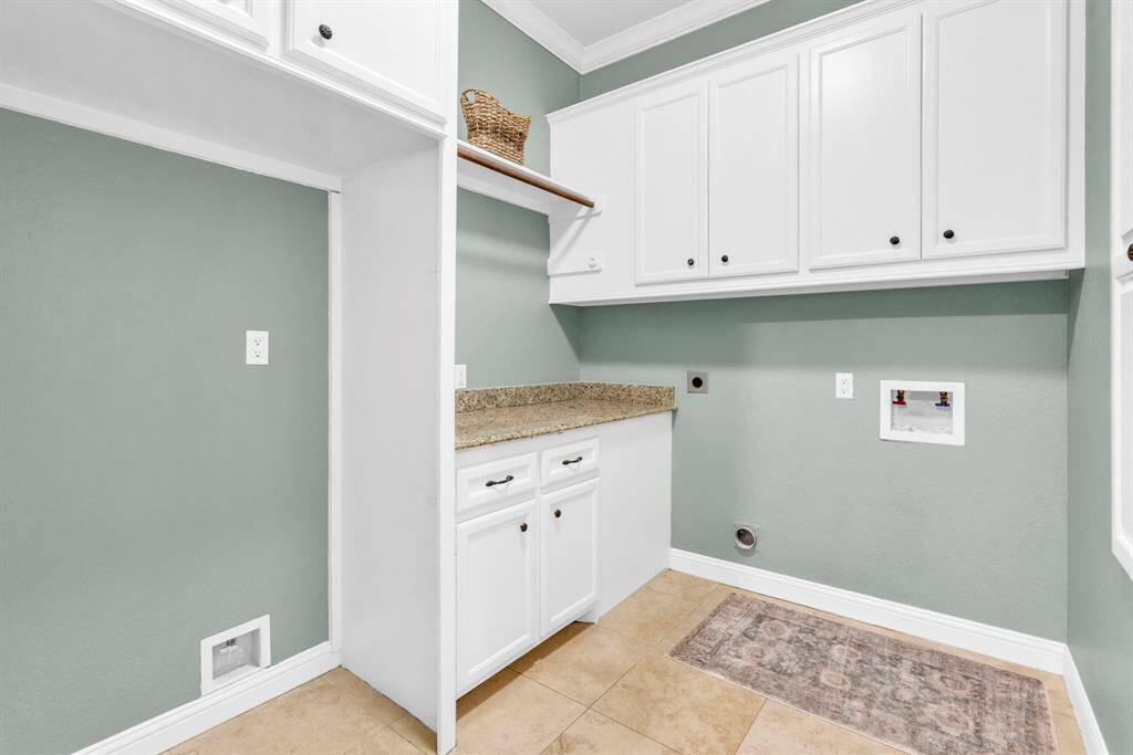 Oversized laundry room outfitted with granite folding counter, wall-to-wall cabinetry, hanging rod, and built-in ironing board—plus ample space for a full-size refrigerator already plumbed for water, turning chore day into an effortless routine.