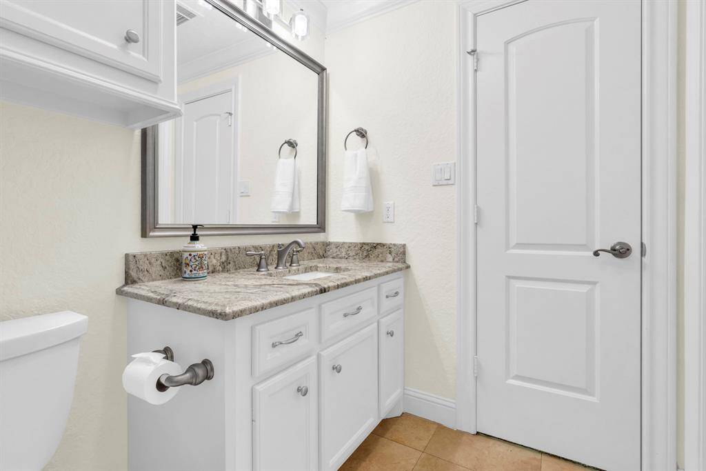 Bright en-suite bath featuring a granite countertop vanity, framed mirror, and upgraded fixtures and cabinetry for extra storage.