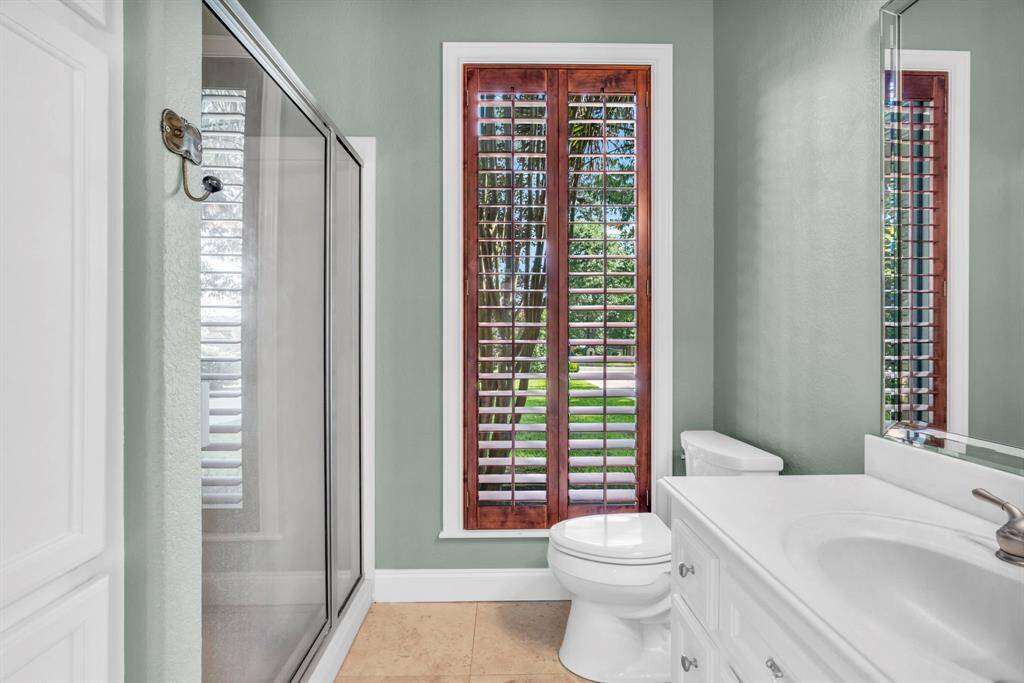 Full bath inside the detached casita, featuring a walk-in shower, crisp white vanity, and plantation-shutter window—perfect for guests enjoying pool-side privacy.