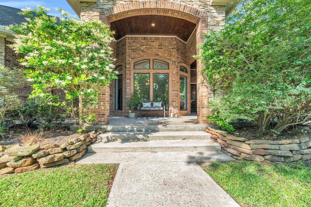 Welcoming arched front porch wrapped in brick and stone features a tongue-and-groove ceiling, twin picture windows, and ample seating space—creating a charming vignette for morning coffee or evening relaxation.