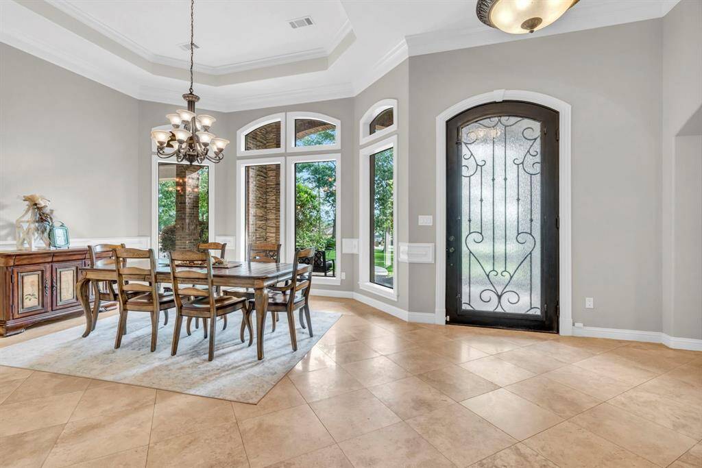 Elegant formal dining room just off the entry showcases a tiered tray ceiling, statement chandelier, and wall of arched windows flanking the wrought-iron front door.
