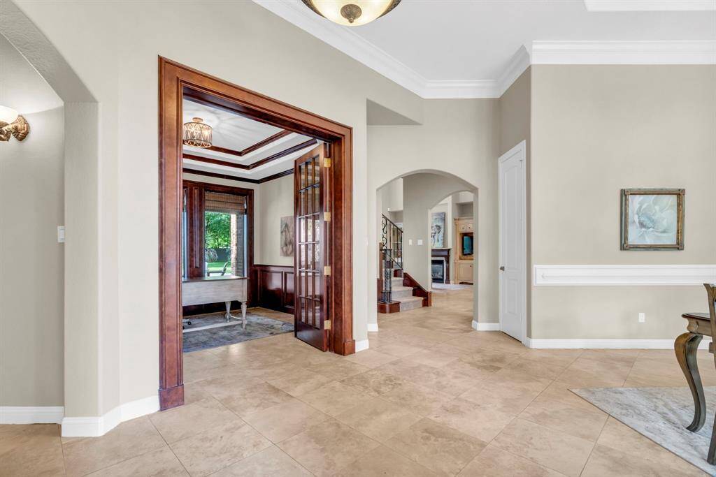 Spacious foyer corridor connects the study, dining room, and great room via graceful arches, crown molding, and neutral tile flooring—creating an inviting sense of openness the moment you enter.