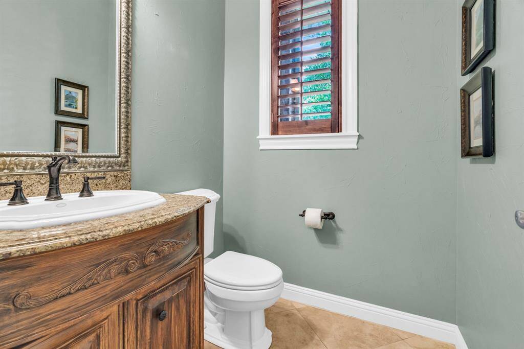 Charming powder bath for guests, featuring a furniture-style curved vanity with detailed woodwork, granite countertop, framed mirror, and a plantation-shutter window that provides both privacy and soft daylight.