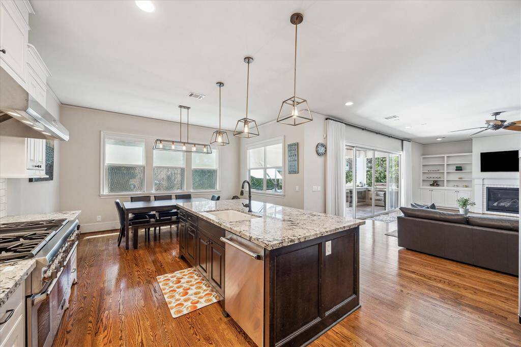 This alternate angle highlights the kitchen’s seamless connection to the living and outdoor spaces, offering an open-concept flow ideal for entertaining. The oversized island, equipped with a deep basin sink and ample counter space, is illuminated by modern pendant lighting. Abundant natural light pours in through large windows and sliding doors, enhancing the airy feel and providing a clear view to the covered patio and pool beyond.