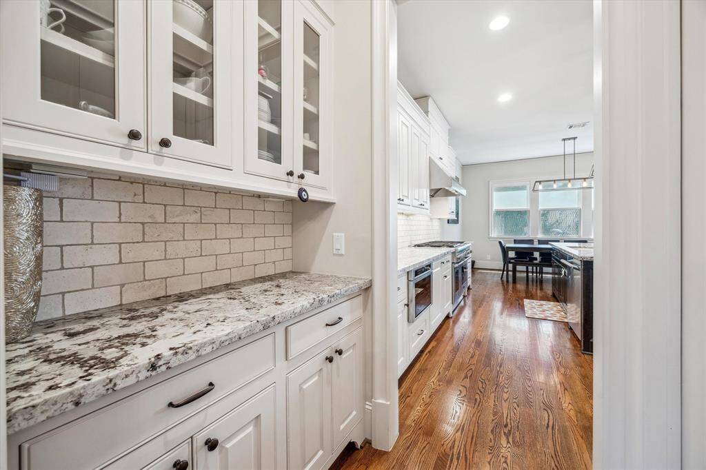 A beautifully appointed butler’s pantry offers extended counter space, abundant cabinetry, and elegant glass-front uppers ideal for display or storage. Granite countertops and a classic subway tile backsplash add texture and timeless charm, while the seamless flow into the kitchen enhances both everyday use and entertaining ease.