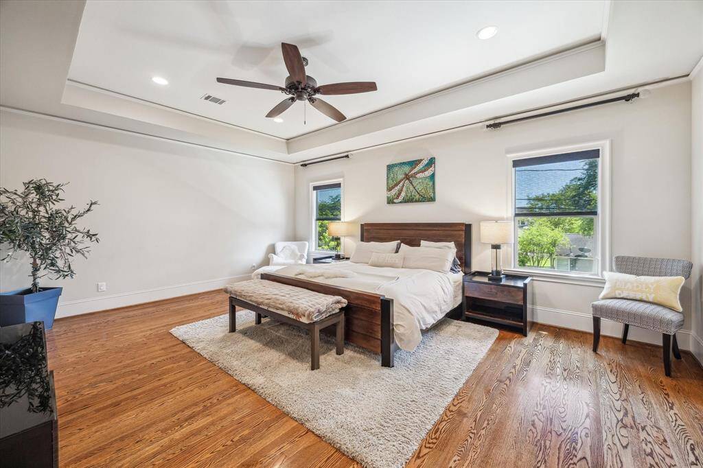 Serene and spacious, the primary suite features rich hardwood floors, a recessed tray ceiling with crown molding, and abundant natural light from dual windows overlooking the treetops. Soft neutral tones create a calming atmosphere, while the generous layout offers ample room to personalize and unwind in comfort.
