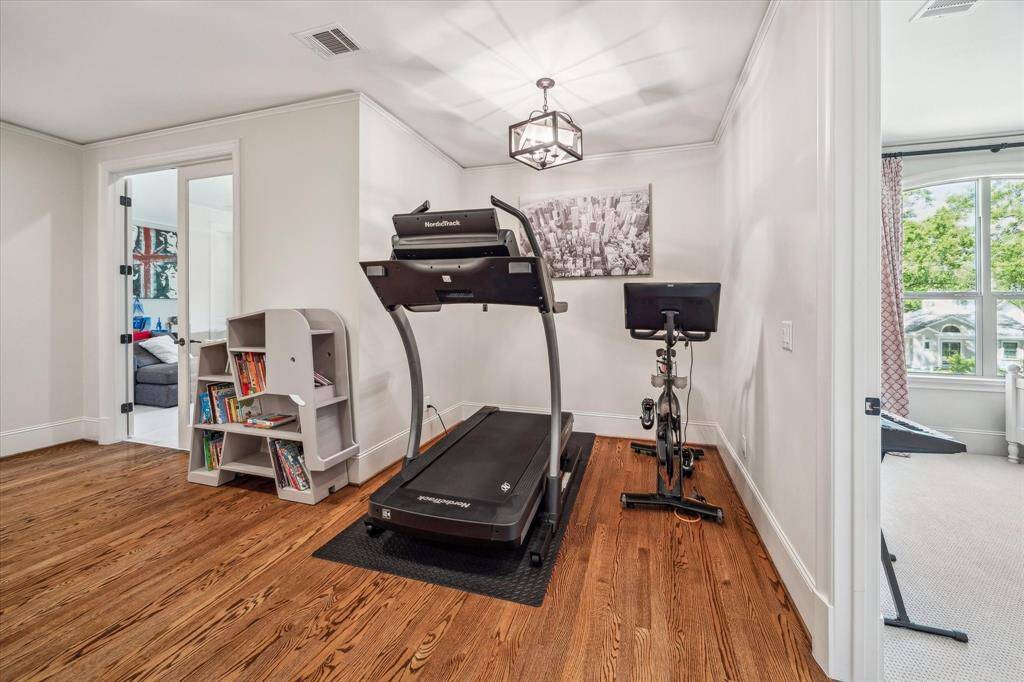 Versatile upstairs nook offers the perfect space for a home gym, reading corner, or study area. Crisp white walls, crown molding, and warm hardwood flooring create a clean and polished aesthetic, while the nearby secondary bedrooms and game room enhance its functionality within the floor plan.