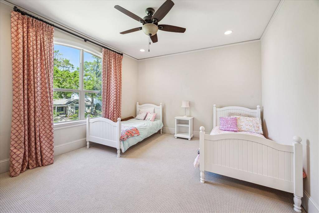 Bright and generously sized secondary bedroom featuring plush carpet, recessed lighting, and a ceiling fan for added comfort. A large arched window frames treetop views and fills the space with natural light, while soft neutral tones offer a calming canvas ready for personalization.