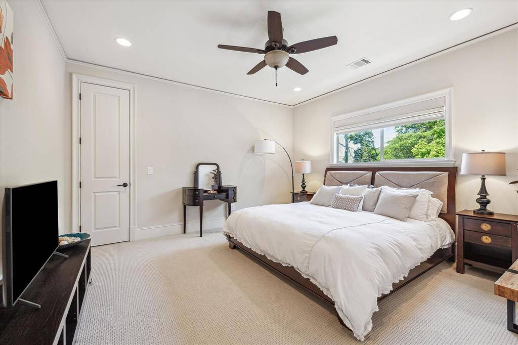 Comfortable and well-proportioned secondary bedroom featuring neutral carpeting, crown molding, and recessed lighting. A wide window frames lush treetop views while bringing in soft natural light, and a ceiling fan adds year-round comfort. The serene palette and clean lines offer flexibility for a variety of uses.