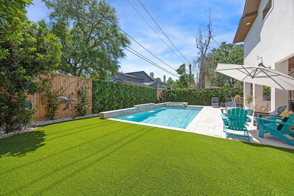 Private backyard retreat featuring a sparkling pool with integrated spa, sleek stone coping, and a serene water feature wall. Surrounded by lush greenery and low-maintenance turf, the outdoor space offers a perfect blend of comfort and privacy.