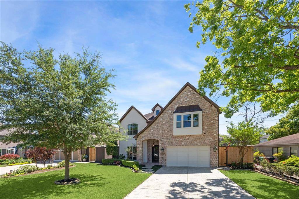 Charming entryway framed by a classic brick arch and accented with warm lantern-style lighting. A wrought iron and glass front door adds a touch of elegance, while the thoughtfully landscaped path invites you in with lush greenery, manicured hedges, and vibrant seasonal flowers.