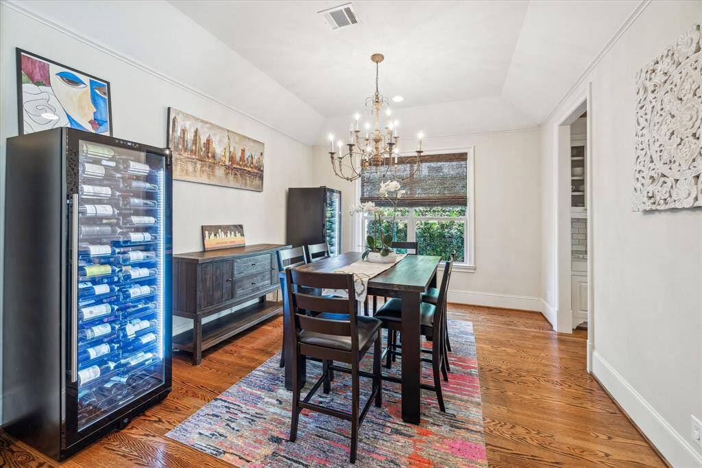 Elegant and inviting, the formal dining room features warm hardwood flooring, a dramatic vaulted ceiling, and a statement chandelier that adds a touch of classic sophistication. Ample natural light filters through woven wood shades.