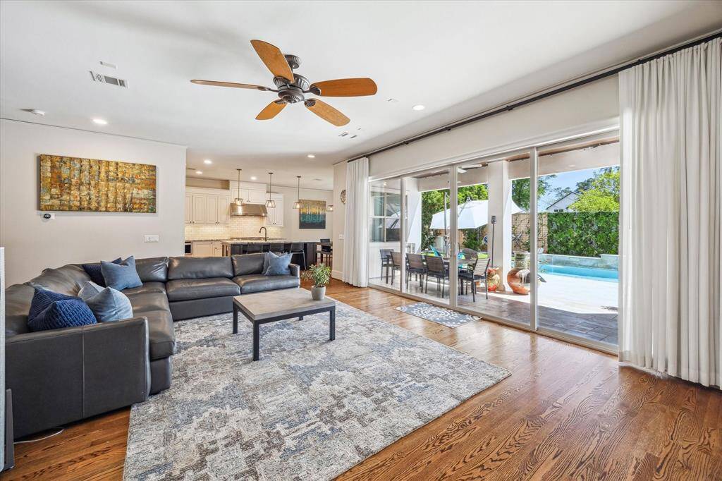 Expansive sliding glass doors create a seamless indoor-outdoor connection, offering direct access to the covered patio and pool area beyond. The open-concept layout flows effortlessly into the kitchen, highlighted by pendant lighting and sleek finishes. Natural light fills the space, enhancing the clean lines and inviting atmosphere of this thoughtfully designed main living area.