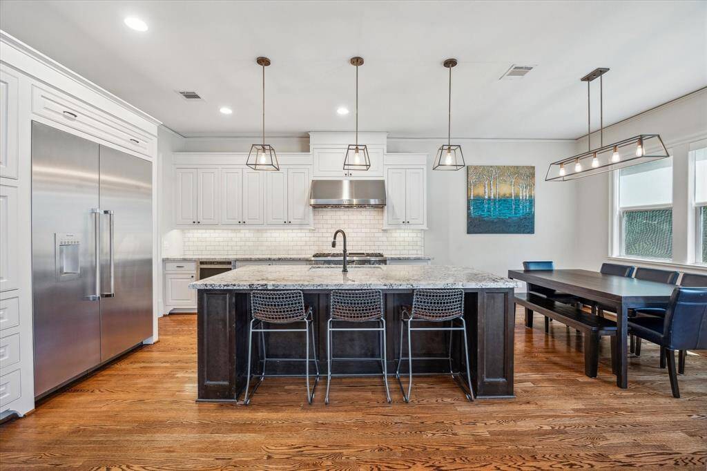 A chef-inspired kitchen showcases clean lines, timeless finishes, and exceptional functionality. Crisp white cabinetry pairs beautifully with the subway tile backsplash and stainless steel appliances, including a built-in refrigerator and commercial-grade range. The expansive island, topped with granite and accented by pendant lighting, provides generous prep space and a stylish focal point.
