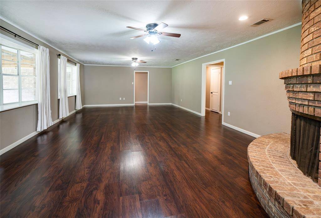 Spacious living room with , neutral walls, large windows with natural light, and a cozy brick fireplace. Ceiling fans enhance comfort in this inviting space.
