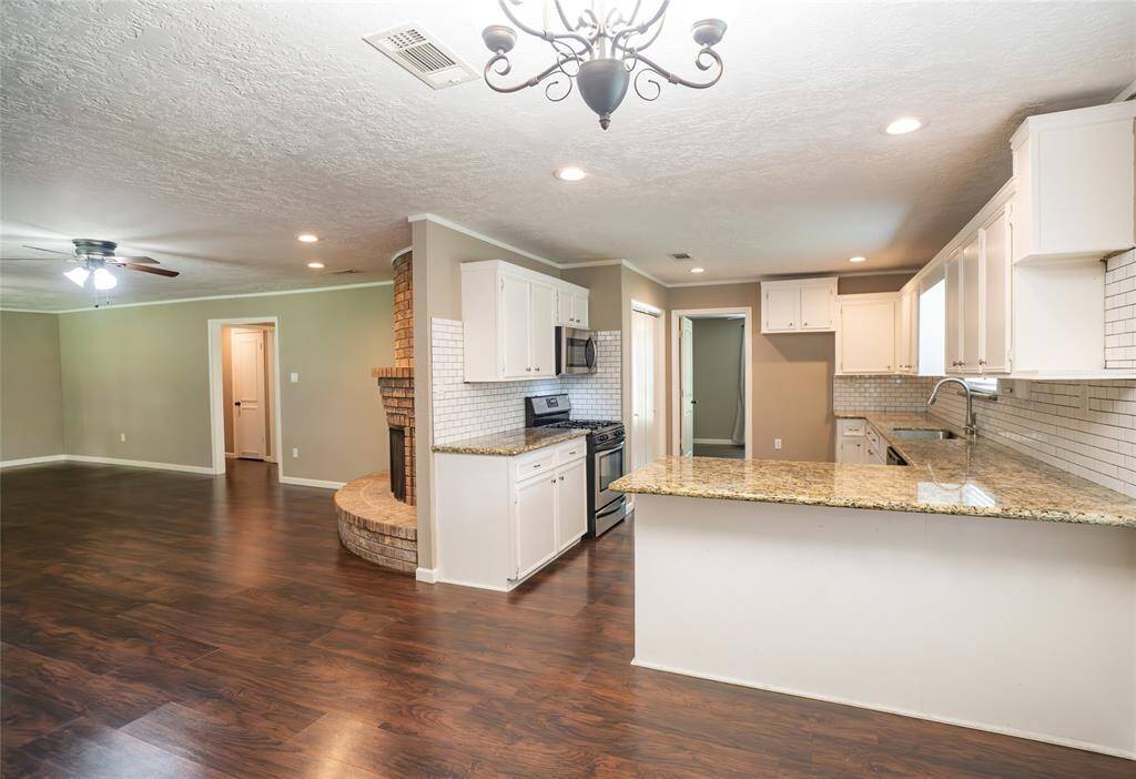 This spacious open-concept living area features a modern kitchen with granite countertops. The room is well-lit with recessed lighting and a stylish chandelier in breakfast, offering a warm and inviting atmosphere.
